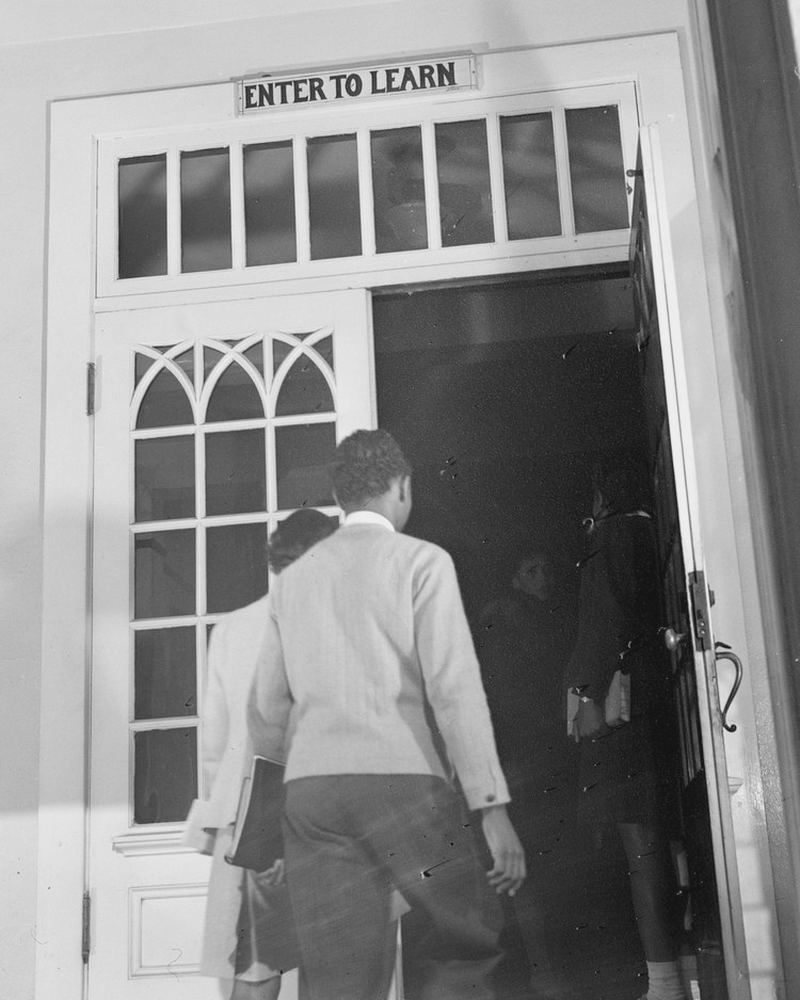 Two students walk through an open doorway under a sign that reads Enter to Learn.