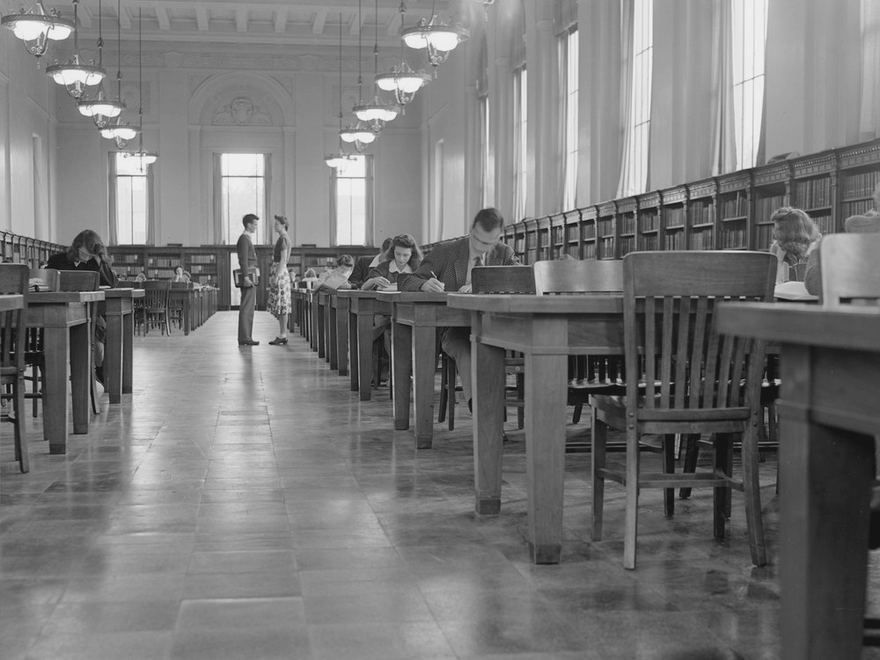 Students reading at long tables in a college library reading room.